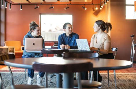 Three people with laptops sit around a table