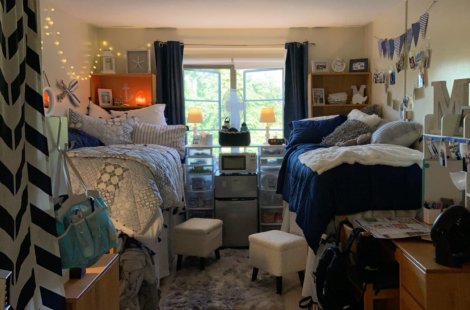 A shared dorm room with two lofted beds on opposite sides, each decorated with patterned bedding and pillows.