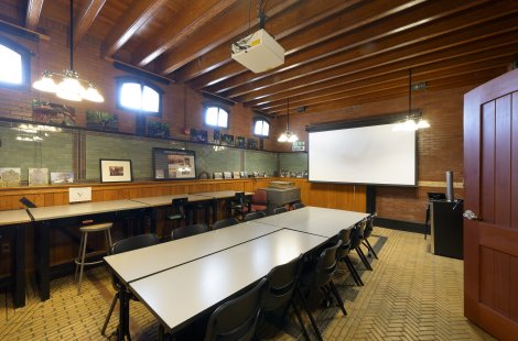 A classroom with a large conference table and a media screen.