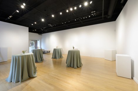 An art gallery with white walls set up for a party with cocktail tables.