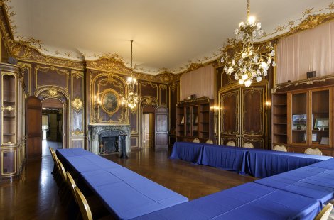 A large ornate room with high ceilings set with a U-shaped conference table and chairs.