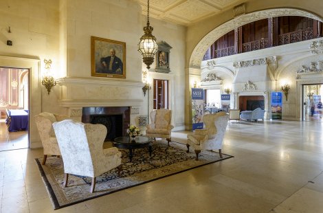 The interior of a stately mansion with grand fireplaces and large pieces of furniture.