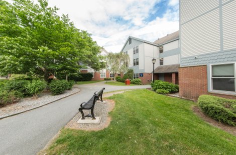 Three-story residential building with light siding, brick lower walls and trees in front.