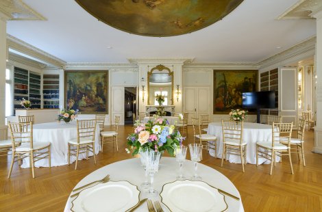 A large ballroom with ornate walls, set with small cocktail tables and chairs.