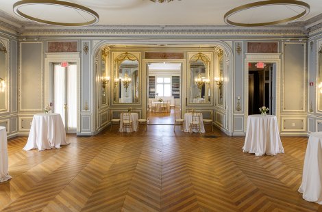 A large ballroom with ornate walls, set with small cocktail tables and chairs.