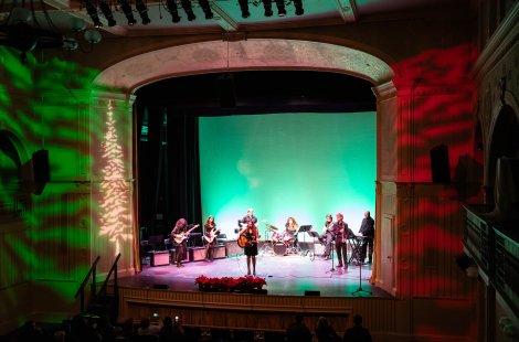 Wide view of a band performing on a theater stage under green and red lighting.