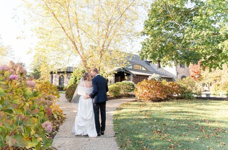 A bride and groom embrace along a pathway leading to a stone and single chapel.