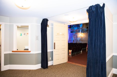 Lobby area leading into a theater auditorium, with an open door, dark curtains and a ticket window on the left.