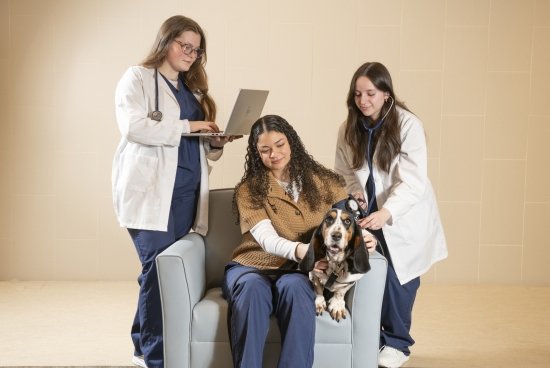Nursing students sitting and standing, running 'tests' on dog for photoshoot image.