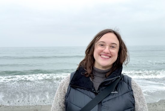 Photo of Brennan at the beach, smiling in a turtleneck and vest.