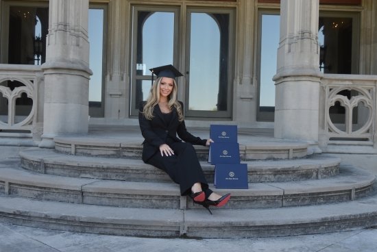 Megan wearing her grad cap on the back steps of Ochre Court, sitting with her three degrees from Salve.