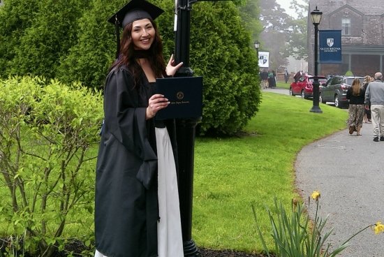 Acevedo wearing her full regalia, holding her diploma smiling next to a lamppost with Salve's logo/flag