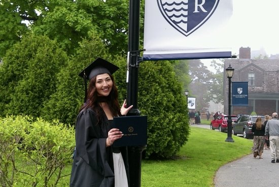 Acevedo wearing her full regalia, holding her diploma smiling next to a lamppost with Salve's logo/flag