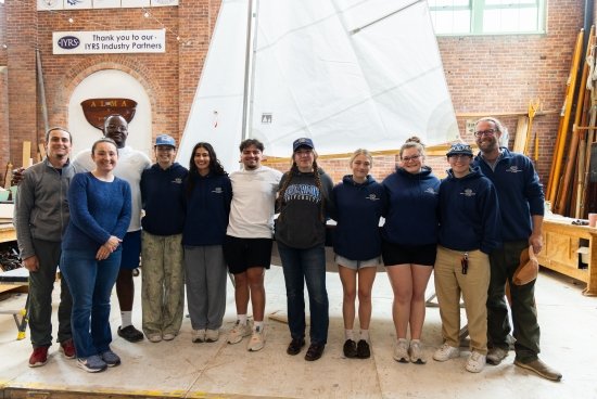 Group photo of the students and instructors in front of the boat they built from the ground up.