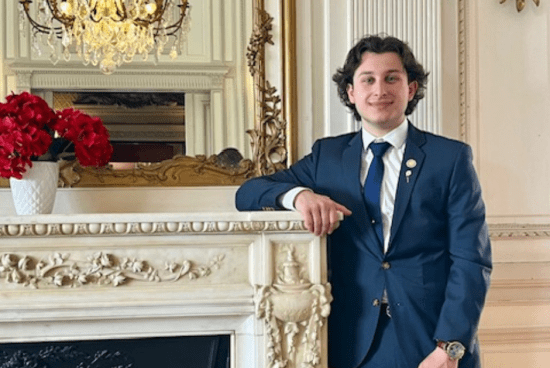 Photo of Silva in a suit smiling and leaning against a white fireplace mantle.