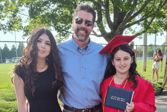 Corey smiling next to his daughters at a high school graduation.