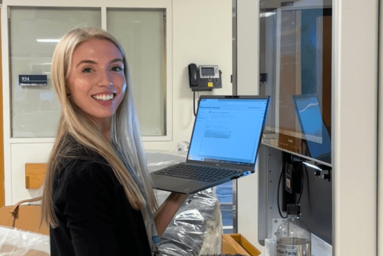 Cara working at the hospital smiling toward camera holding a computer.