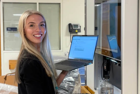Cara working at the hospital smiling toward camera holding a computer.