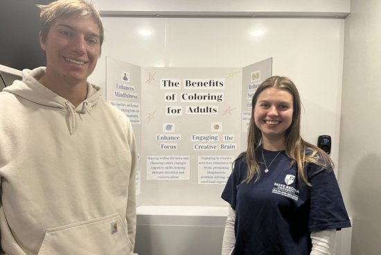 Anderson and man standing in front of a poster board smiling.