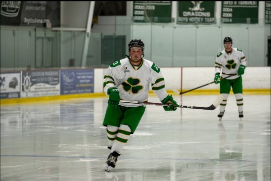Connolly on the ice rink in his green and white hockey uniform, holding his stick.