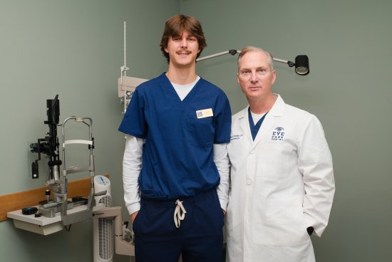 Optometrist and intern standing in eye exam room posing for photo.