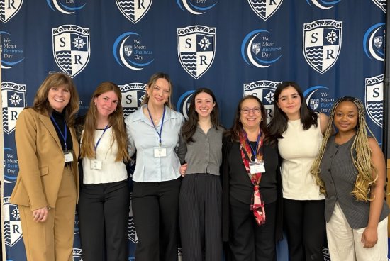 Jessicka and other students smiling in front of a We Mean Business Day backdrop.