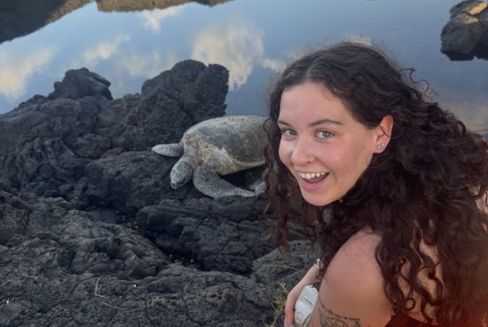 Bermingham smiling on rocks next to a sea turtle.