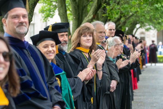 faculty in their regalia clapping as students walk down to graduation.