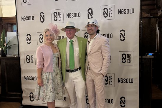 group photo of three people in pink and green outfits in front of a NOSOLO backdrop, for a Kentucky Derby fundraising event.