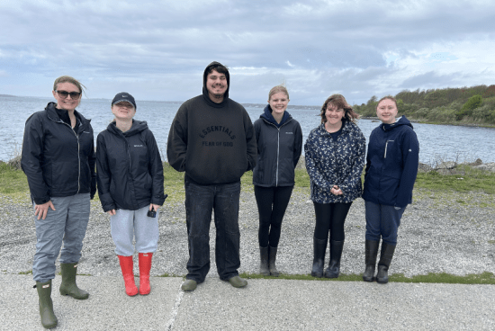 group photo of six people outside in front of the ocean.