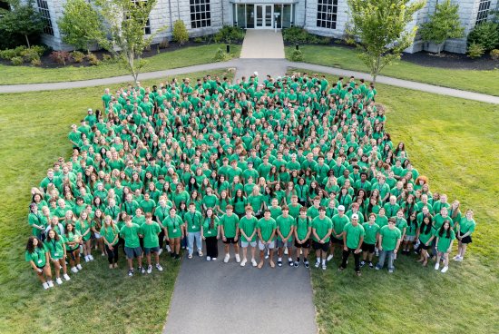 Students in green shirts gather for a large group photo on campus.
