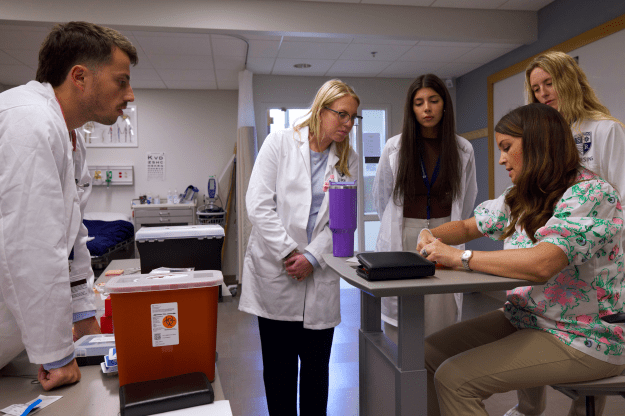 Graduate nursing students watching instructor demonstrate how to do sutures.