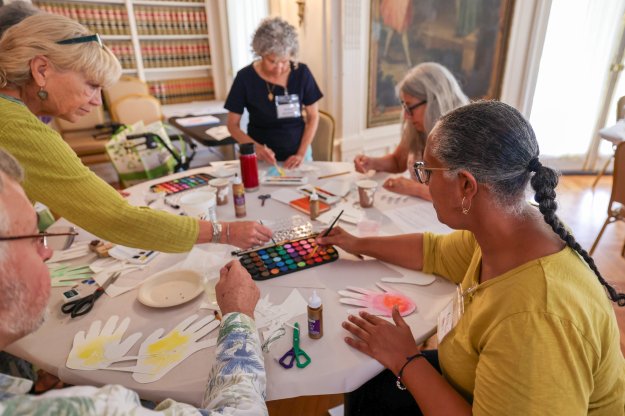 A table of expressive arts graduate students participating in an art workshop. The group is sharing a large paint palette and other craft supplies.
