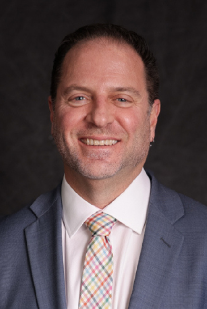 Professional headshot of Lorenz smiling in grey suit and colorful plaid tie.