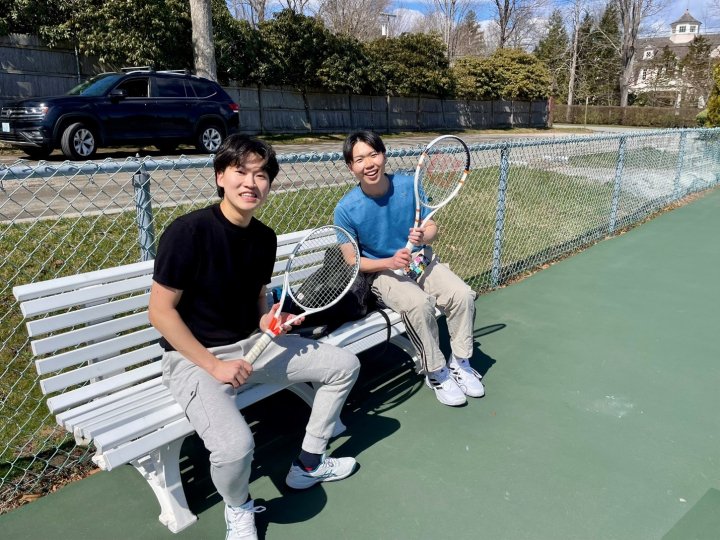 Two males on a bench holding tennis rackets