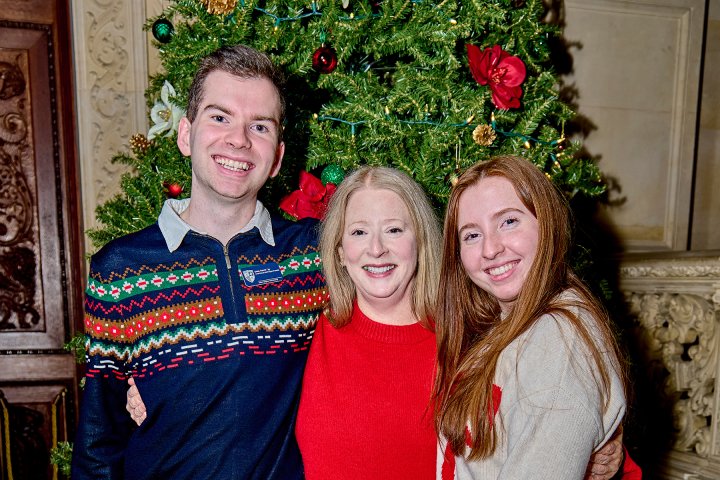 A man and two women pose together in front of a decorated Christmas tree.