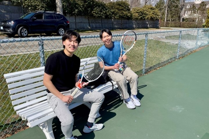 Two males on a bench holding tennis rackets