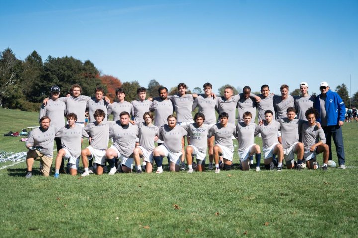 A group of men’s rugby players pose in two rows on a grassy field.