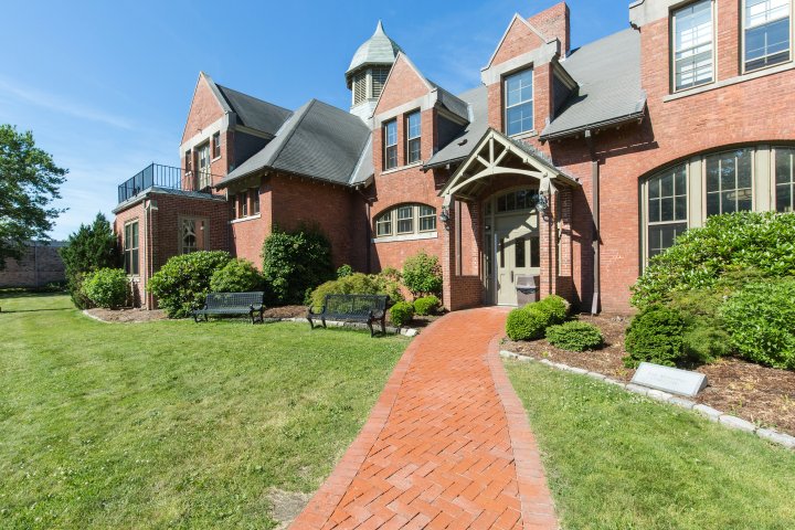 Exterior of a red brick building with a gabled roof, arched entrance and a brick walkway leading to the front door.