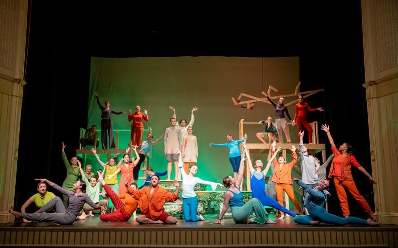 Large cast of actors in bright colored costumes in energetic poses