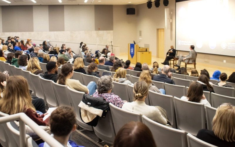 An audience listens to speakers on stage in an auditorium