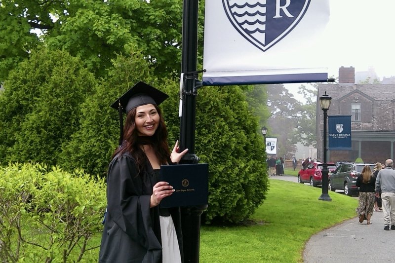 Acevedo wearing her full regalia, holding her diploma smiling next to a lamppost with Salve's logo/flag