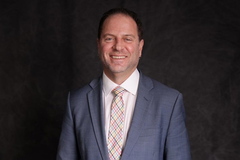 Professional headshot of Lorenz smiling in grey suit and colorful plaid tie.