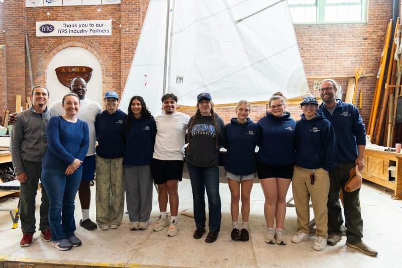 Group photo of the students and instructors in front of the boat they built from the ground up.