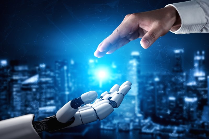 Human hand and robot hand reaching toward each other with futuristic blue background.