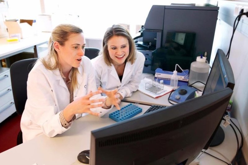 Jillian Wise and another collegue sitting in white lab coats discussing something they are viewing on the computer in front of them.