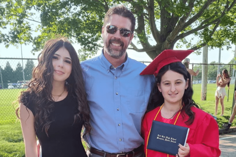 Corey smiling next to his daughters at a high school graduation.