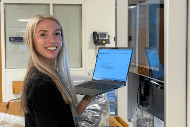 Cara working at the hospital smiling toward camera holding a computer.