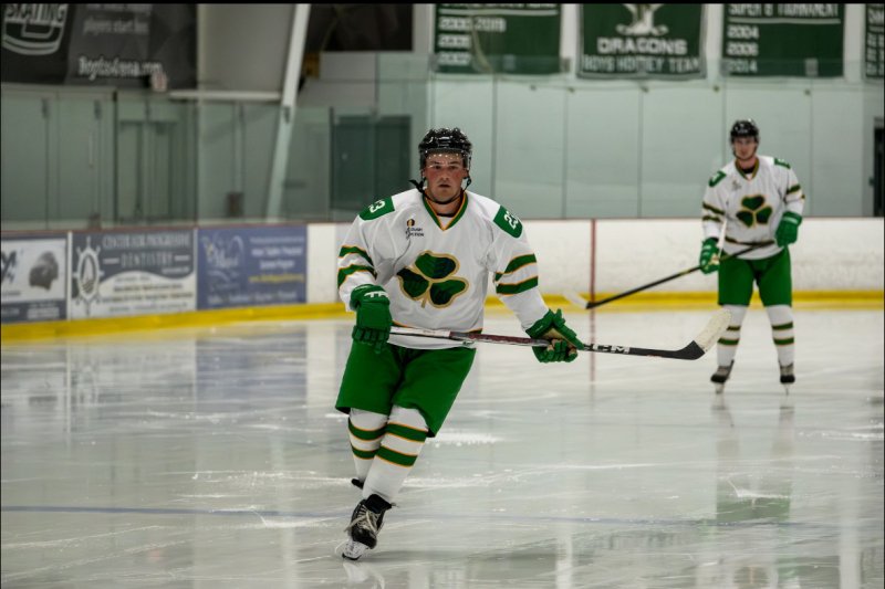 Connolly on the ice rink in his green and white hockey uniform, holding his stick.