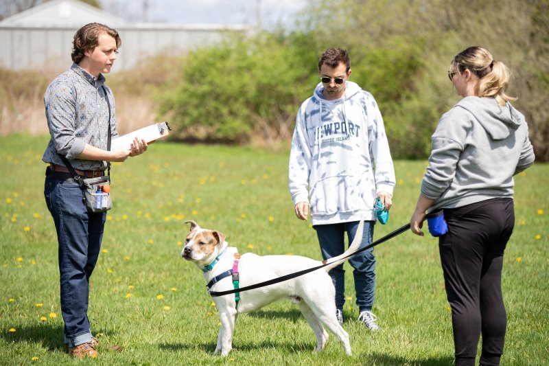 two students and professor outside in field, one with a white and tan dog on a leash.